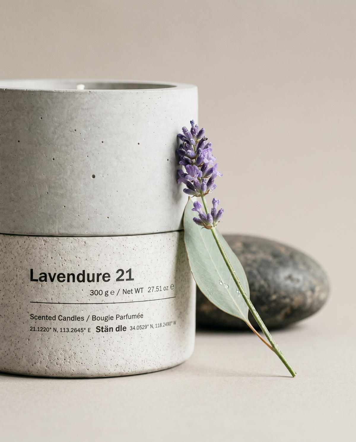 Close-up of the Lavendure 21 concrete vessel and label by Stāndle, with a fresh lavender sprig and a eucalyptus leaf resting against it.