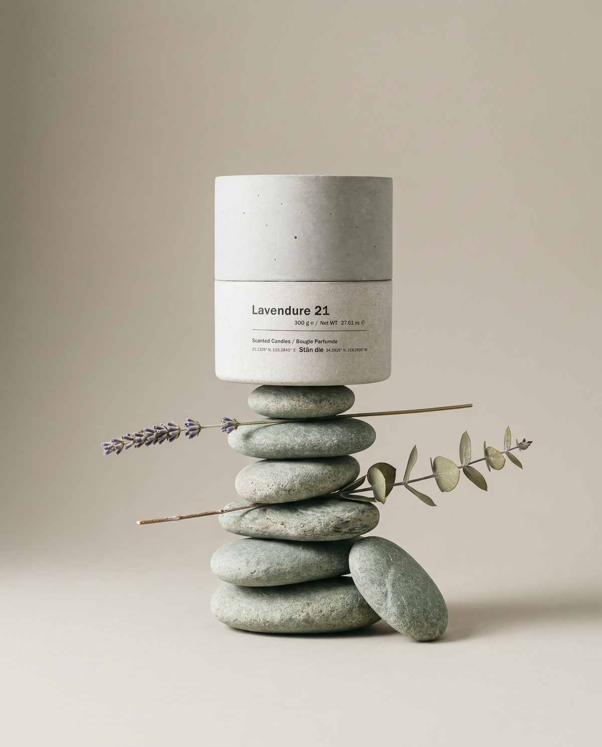 Lavendure 21 lavender and eucalyptus concrete soy candle by Stāndle, balanced on a cairn of grey-green river stones with lavender and eucalyptus sprigs threaded through the stack.