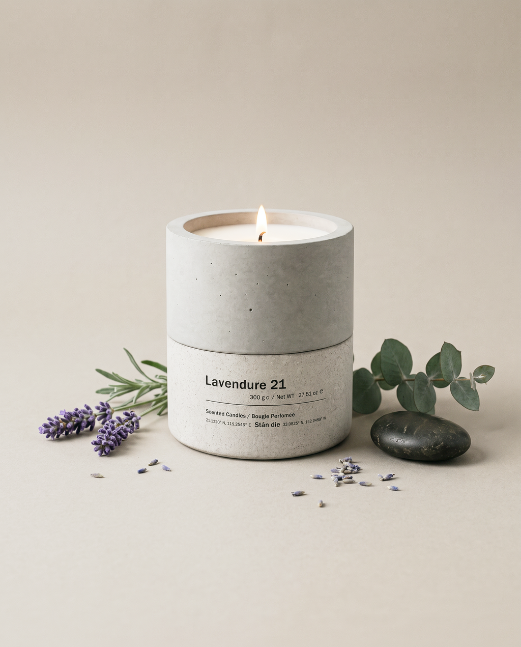 Lavendure 21 lavender and eucalyptus concrete soy candle by Stāndle, lit, beside a lavender sprig, eucalyptus, and a smooth dark river stone.