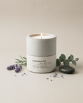 Lavendure 21 lavender and eucalyptus concrete soy candle by Stāndle, lit, beside a lavender sprig, eucalyptus, and a smooth dark river stone.