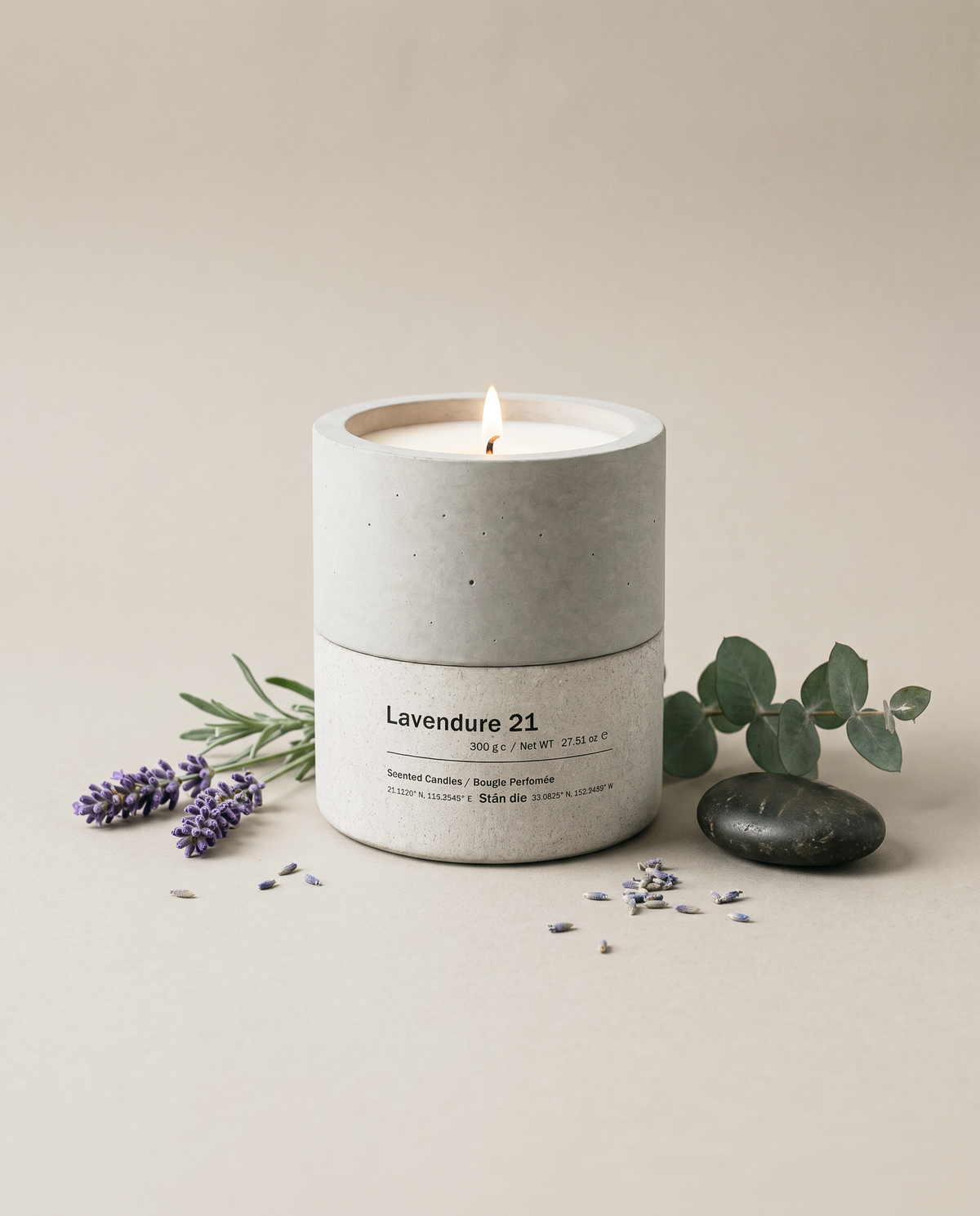 Lavendure 21 lavender and eucalyptus concrete soy candle by Stāndle, lit, beside a lavender sprig, eucalyptus, and a smooth dark river stone.