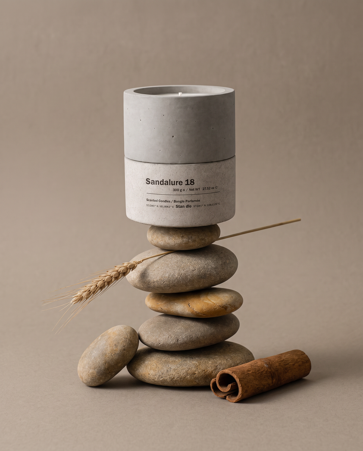 Sandalure 18 sandalwood and vanilla concrete soy candle by Stāndle, lit, beside a cinnamon stick, vanilla pods, pale sandalwood pieces, and a dark river stone.