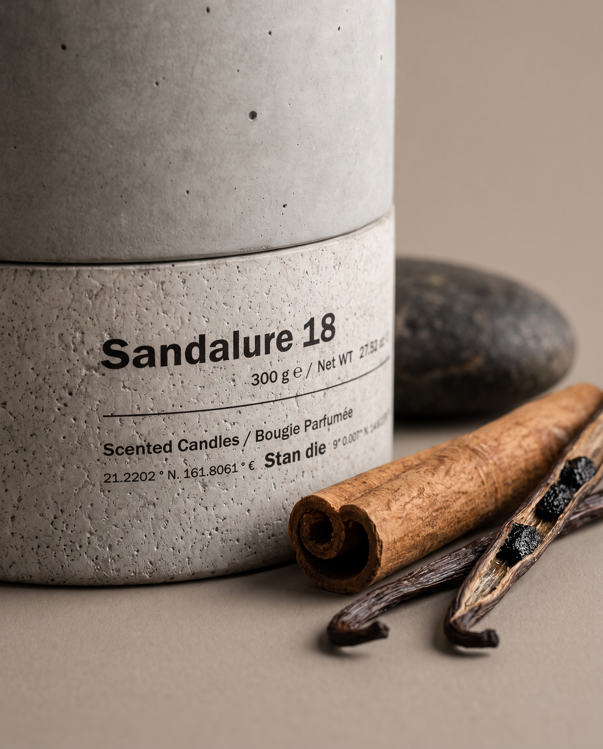 Close-up of the Sandalure 18 concrete vessel and label by Stāndle, with a cinnamon stick and split vanilla pods resting against it.