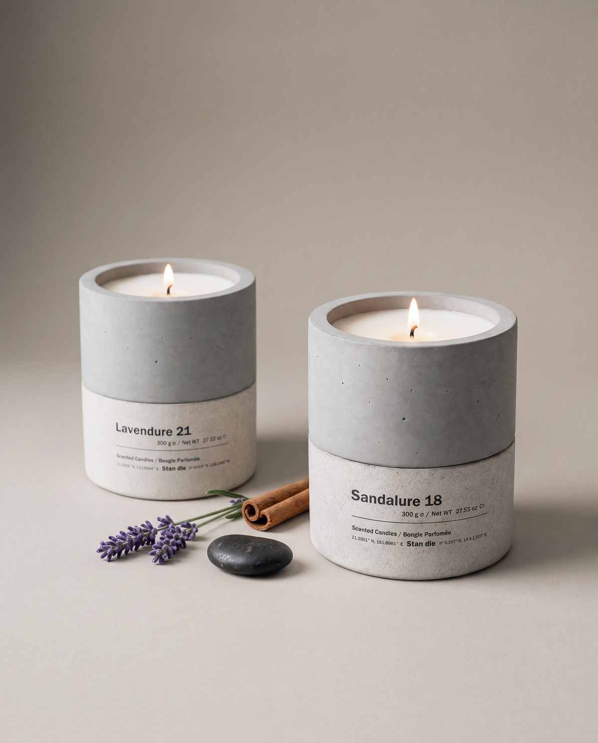 Stāndle Duo gift set — Lavendure 21 and Sandalure 18 concrete soy candles, both lit, with a lavender sprig, a cinnamon stick, and a dark river stone.