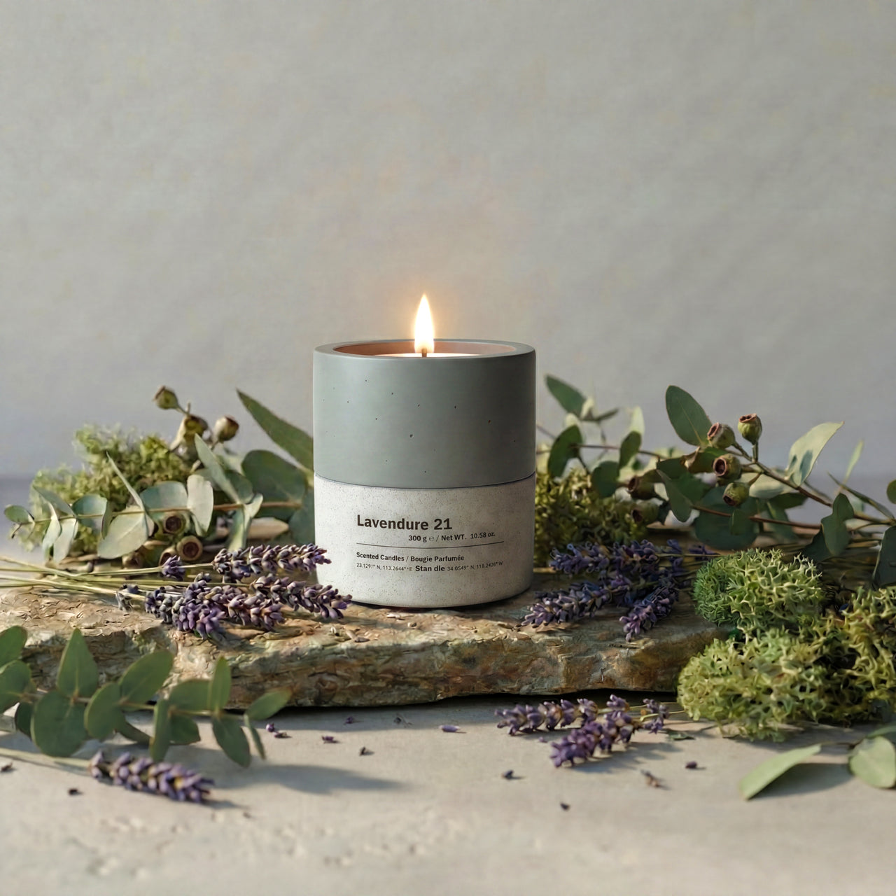 Lavendure 21 scented soy candle in a dual-tone concrete vessel, surrounded by fresh lavender sprigs and eucalyptus branches on a natural stone surface