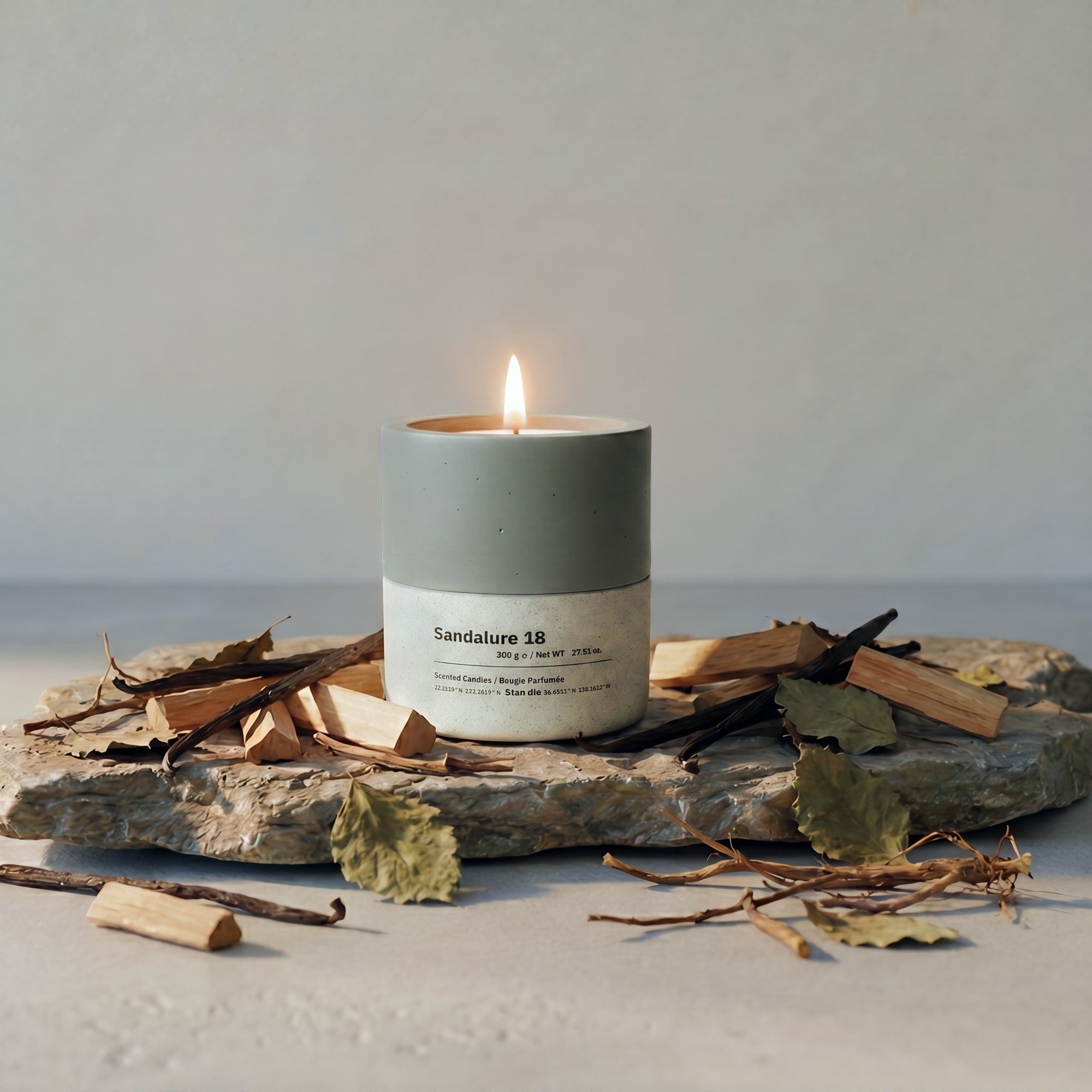 Sandalure 18 sandalwood vanilla soy candle burning in dual-tone concrete vessel, surrounded by sandalwood, vanilla pods and dried Patchouli