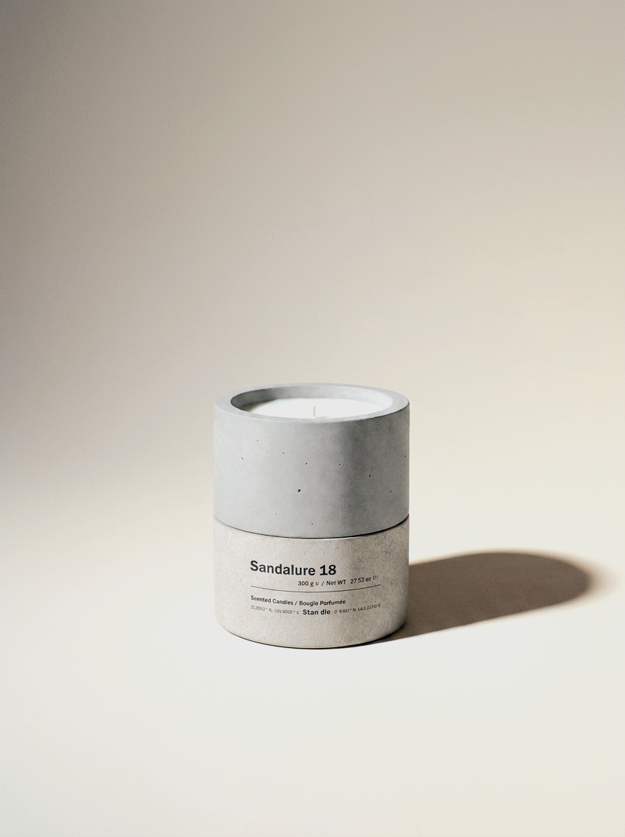 Sandalure 18 sandalwood and vanilla candle — 300g soy wax in a two-tone hand-cast concrete vessel, unlit, on a warm off-white studio backdrop